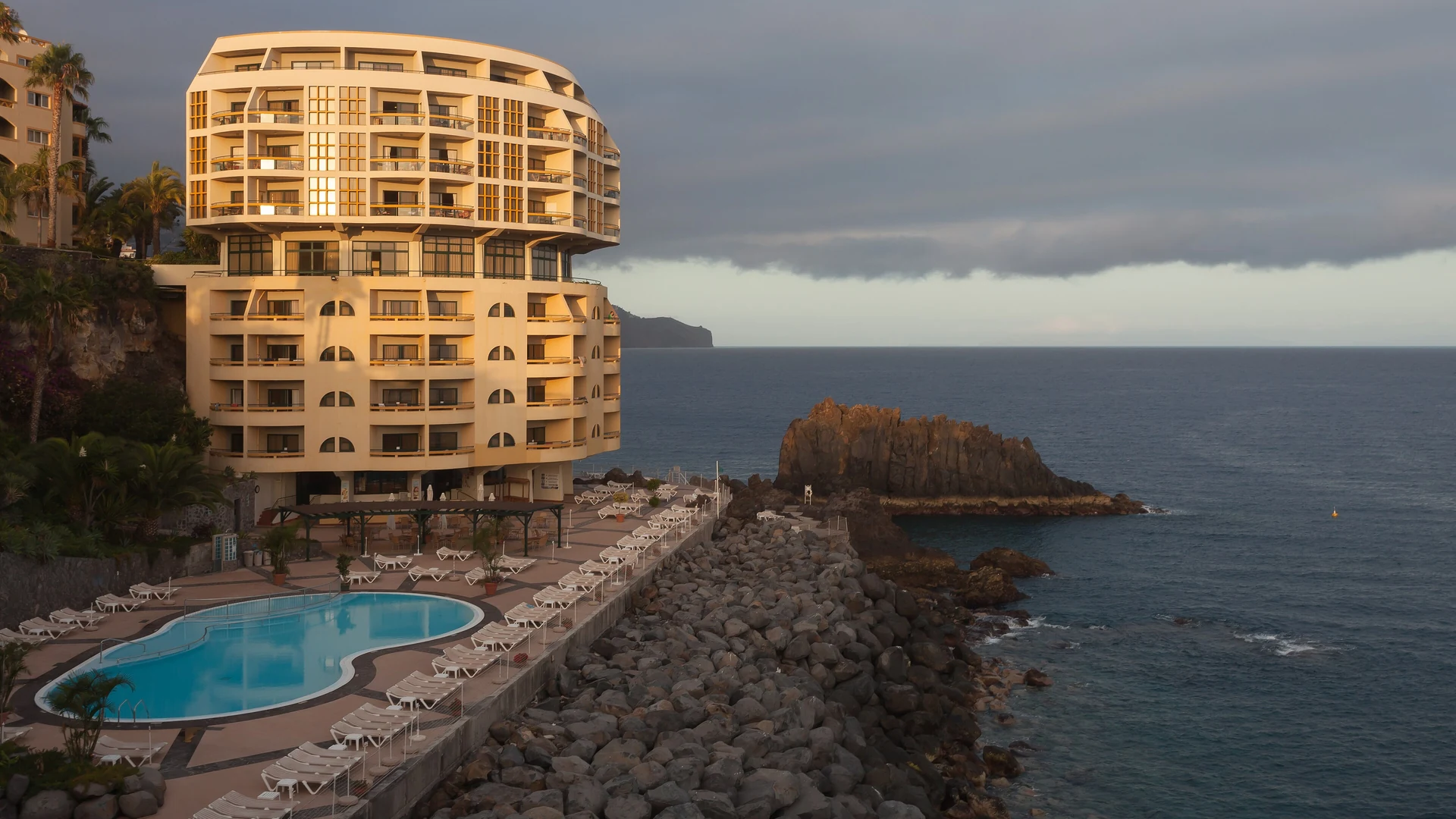 A clifftop hotel and pool deck above the sea at golden hour on the Funchal coast, Madeira
