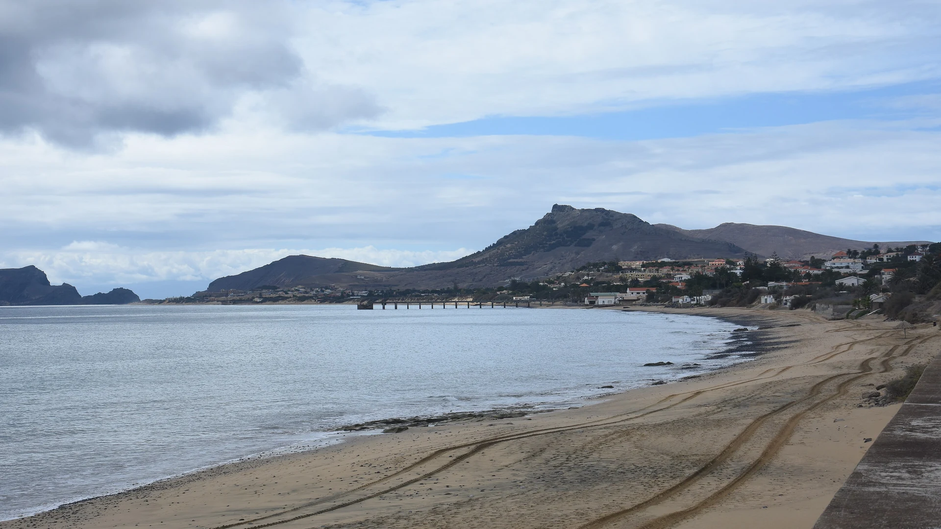 The long golden-sand beach of Porto Santo curving along the bay, with the island's hills and pier behind