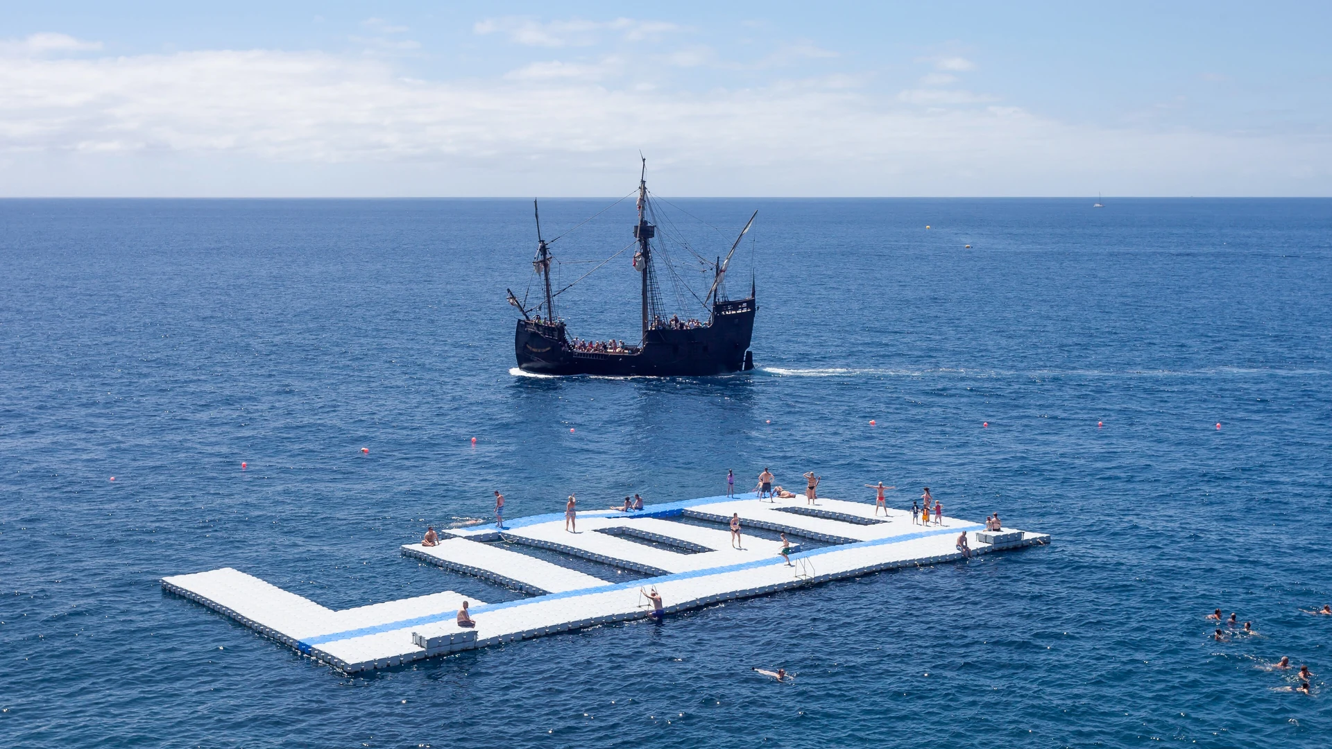 Swimmers at a floating sea platform off the Funchal Lido, with a tall ship beyond, Madeira