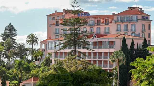 Die rosa Fassade des Hotels Reid's Palace zwischen Palmen oberhalb von Funchal, Madeira