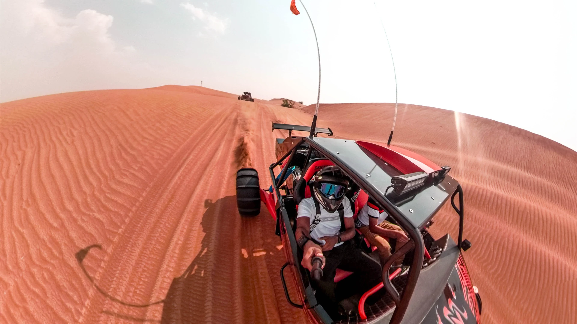 A driver at the wheel of a two-seater off-road buggy kicking up dust on a trail