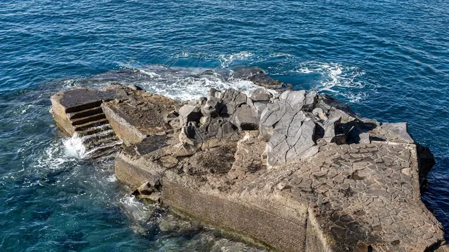 A volcanic-rock natural sea pool on Madeira's coast, waves breaking over the stones on a sunny day