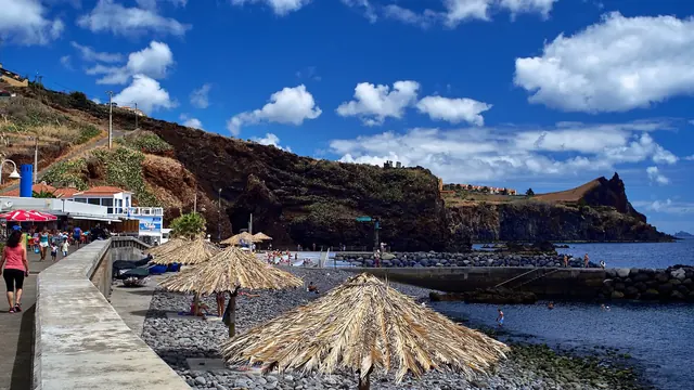 Straw sunshades over a pebble beach at Praia dos Reis Magos on a sunny summer day, Madeira