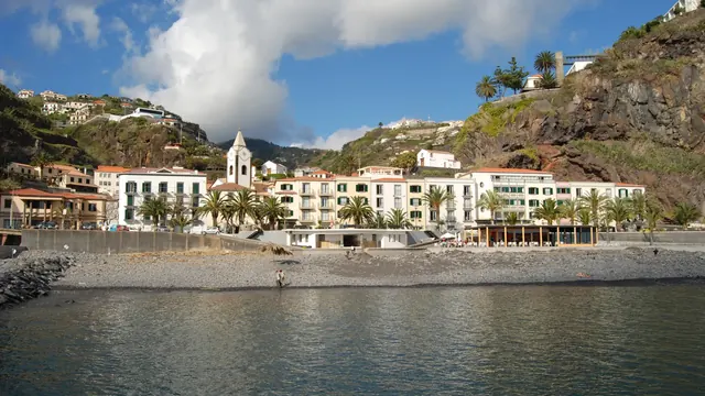 Die sonnige Uferpromenade und der Strand von Ponta do Sol an der Südküste Madeiras unter blauem Himmel