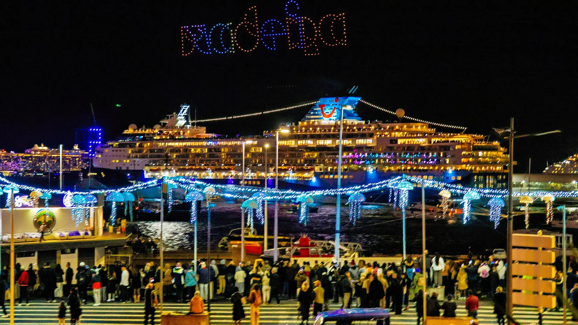 Silvester in Funchal: Drohnenshow mit dem Schriftzug Madeira über dem Hafen, davor ein beleuchtetes Kreuzfahrtschiff und Zuschauer an der Uferpromenade
