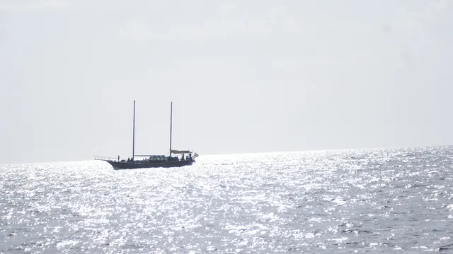 A two-masted sailing boat silhouetted on a sun-glittered sea off Madeira at sunset